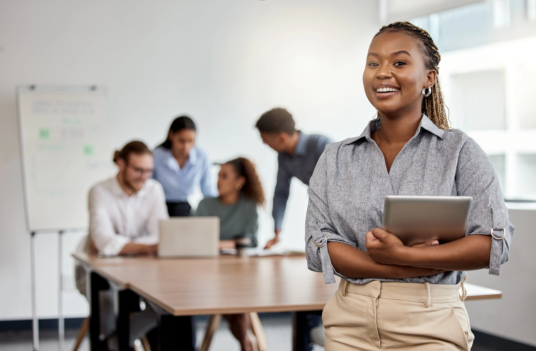 Femme souriante avec PC dans une classe, en fond un groupe de travail