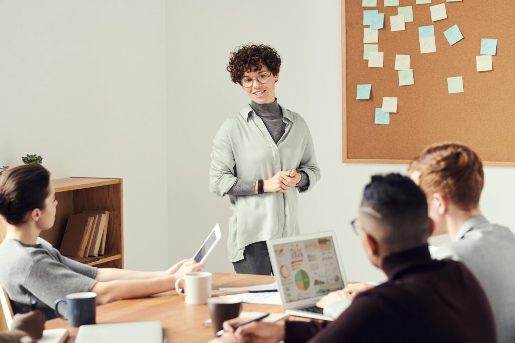 femme debout face à un groupe et devant un tableau de post-it