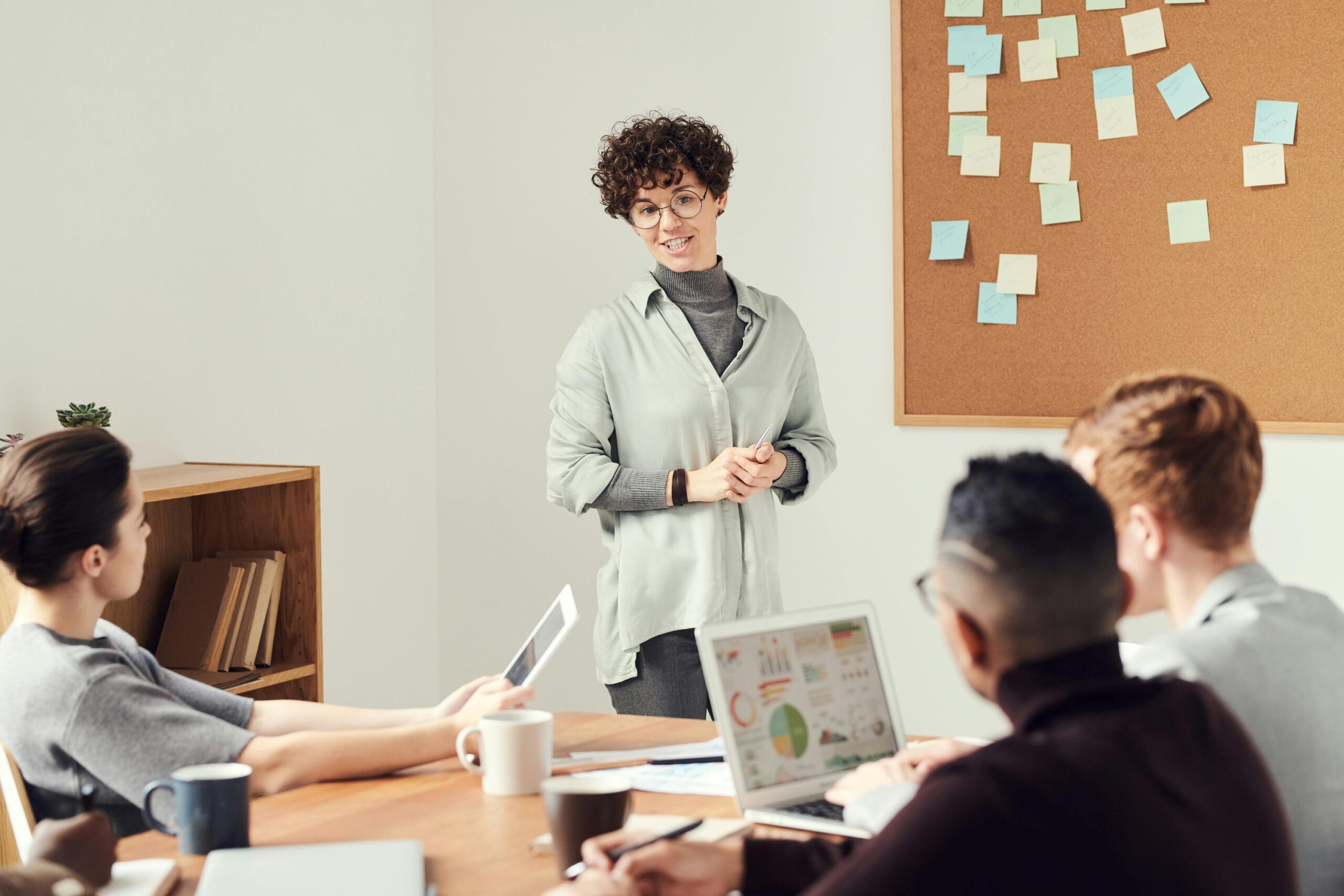 femme debout face à un groupe et devant un tableau de post-it